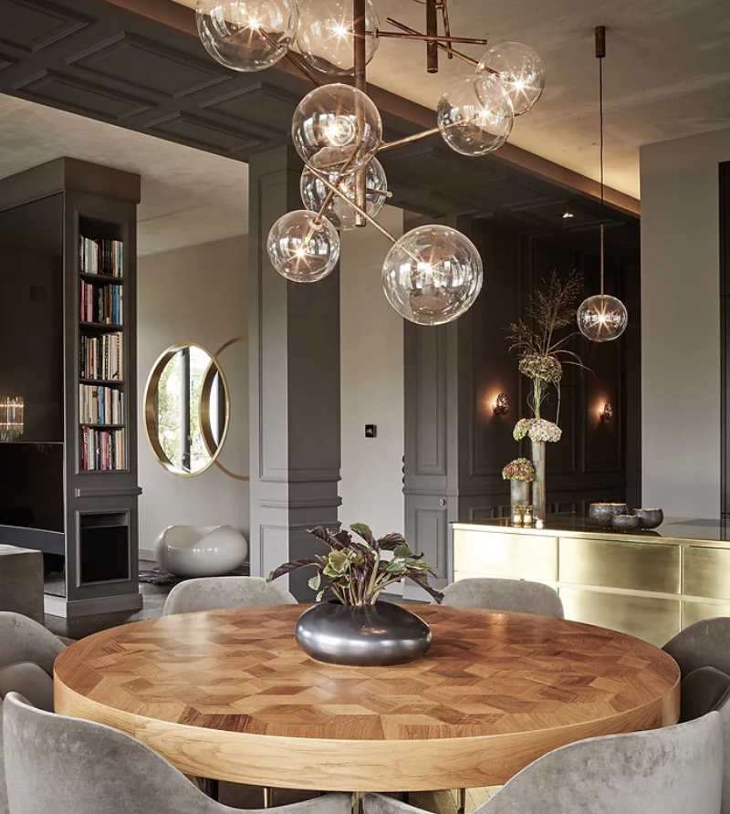 apartment nº eleven light brown dining table with light grey dining chairs around and a chandelier on top.